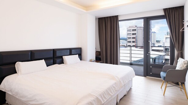 A modern hotel room with a large bed, a balcony with a view of the city, and a seating area with a chair. - Cypress Inn (Taitung)