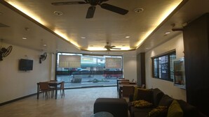 Un hall d’entrée spacieux, doté d’un ventilateur de plafond, d’un téléviseur fixé au mur et offrant une vue sur la rue grâce à de grandes fenêtres.