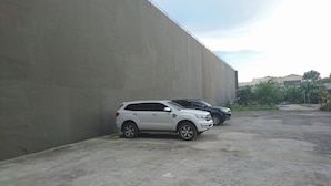 Un espace de stationnement où sont garés un VUS blanc et un VUS noir, le long d’un mur en béton.