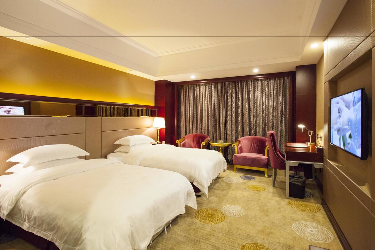 Une chambre d’hôtel avec deux lits, un bureau, une télévision et un rideau.
