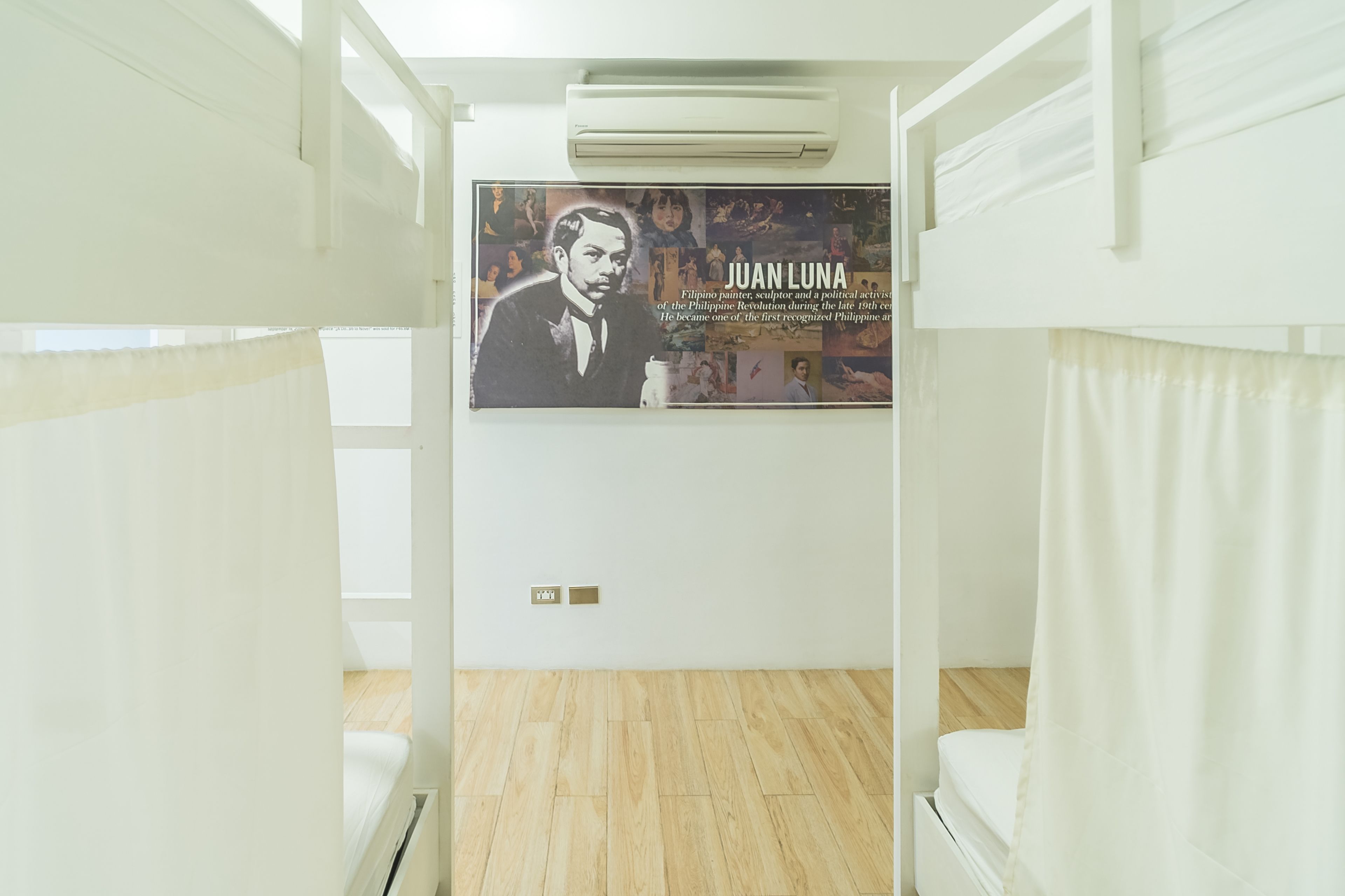 Una habitación de hotel con literas, un cartel de Juan Luna y un equipo de aire acondicionado.