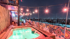 A rooftop hot tub with a city view, surrounded by wooden benches and string lights. - Heroes Hotel (Manila)