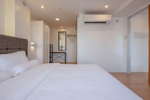 A modern hotel room with a large bed, a bedside table, a mirror, and an air conditioning unit. - Heroes Hotel (Manila)