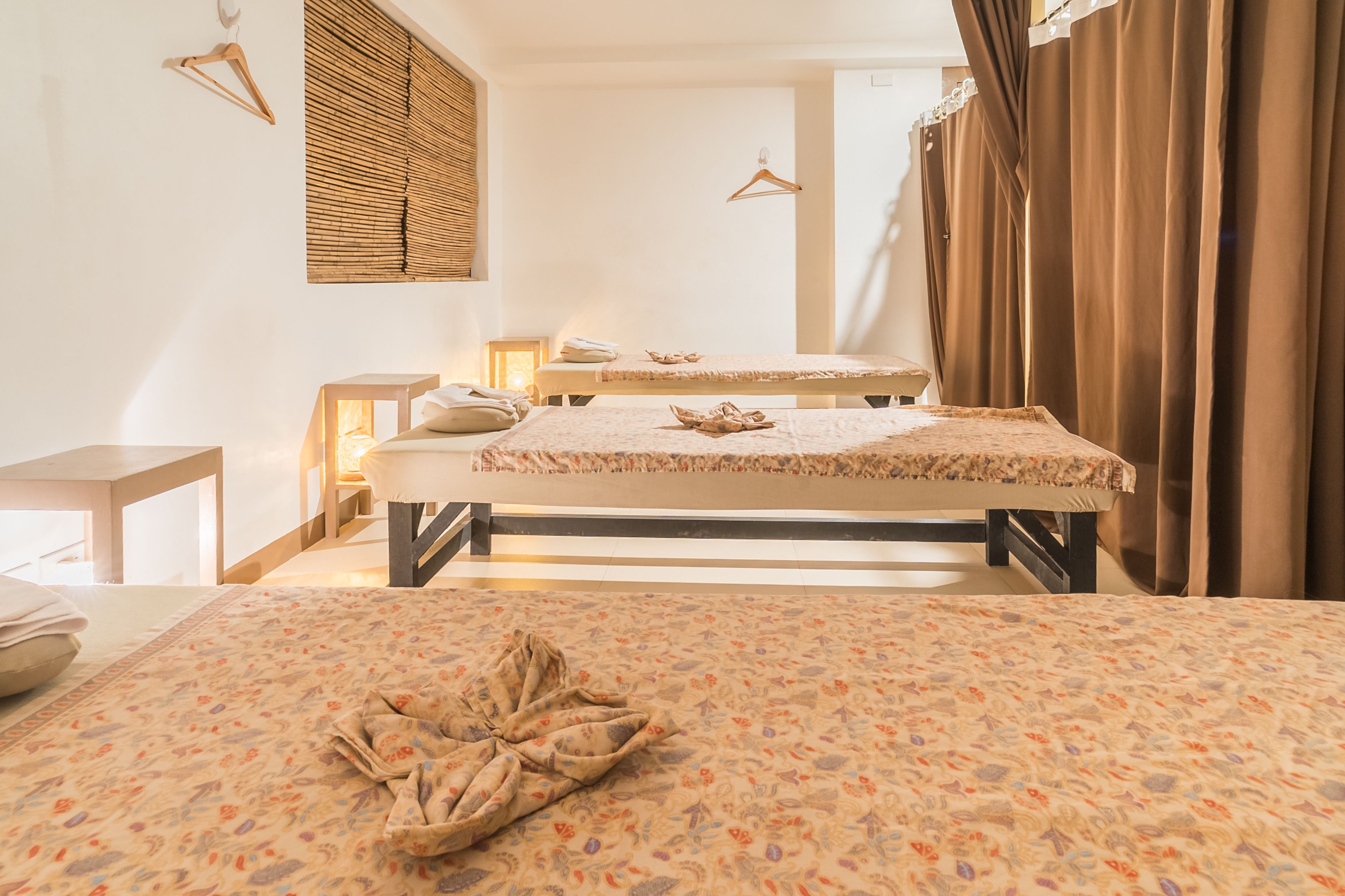Una habitación de hotel con dos camas, un banco de madera, una lámpara colgante y una ventana con persianas.