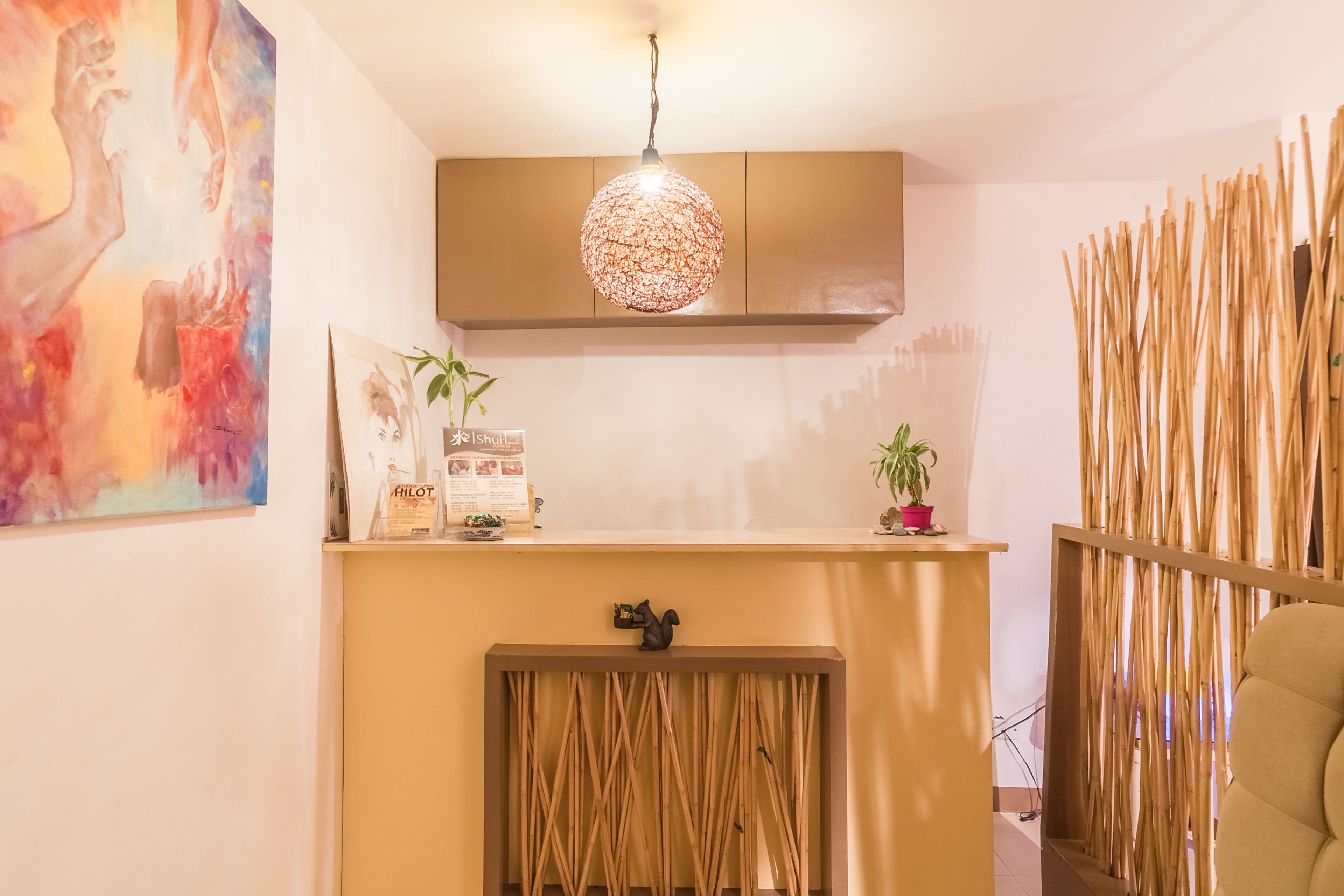 Un comptoir d’accueil agrémenté d’un luminaire sphérique suspendu, d’une œuvre d’art encadrée et d’une petite plante en pot.