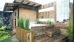 A rustic wooden outdoor seating area with a built-in bench and a small table, surrounded by potted plants and a wooden fence. - Heroes Hotel (Manila)