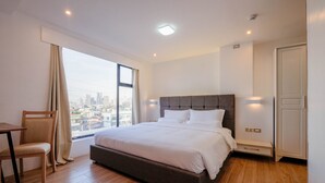 A modern hotel room with a large bed, a desk, and a view of the city. - Heroes Hotel (Manila)