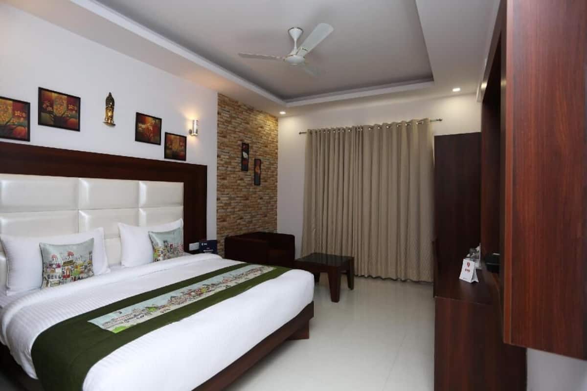 Habitación de hotel con cama, escritorio, silla, armario, ventilador de techo y obras de arte en las paredes.