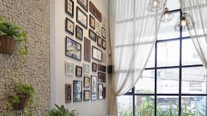 A cozy indoor space with a stone wall, a sofa, a coffee table, and a chair. There are plants and a window with curtains. - Maison De Camille Boutique Hotel (Ho Chi Minh City)