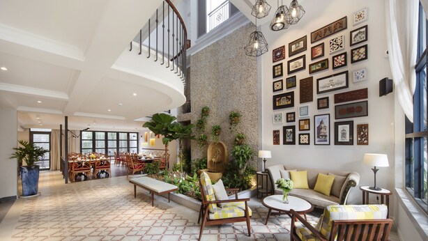 A spacious living area with a high ceiling, a stone wall, and a collection of framed artworks. - Maison De Camille Boutique Hotel (Ho Chi Minh City)