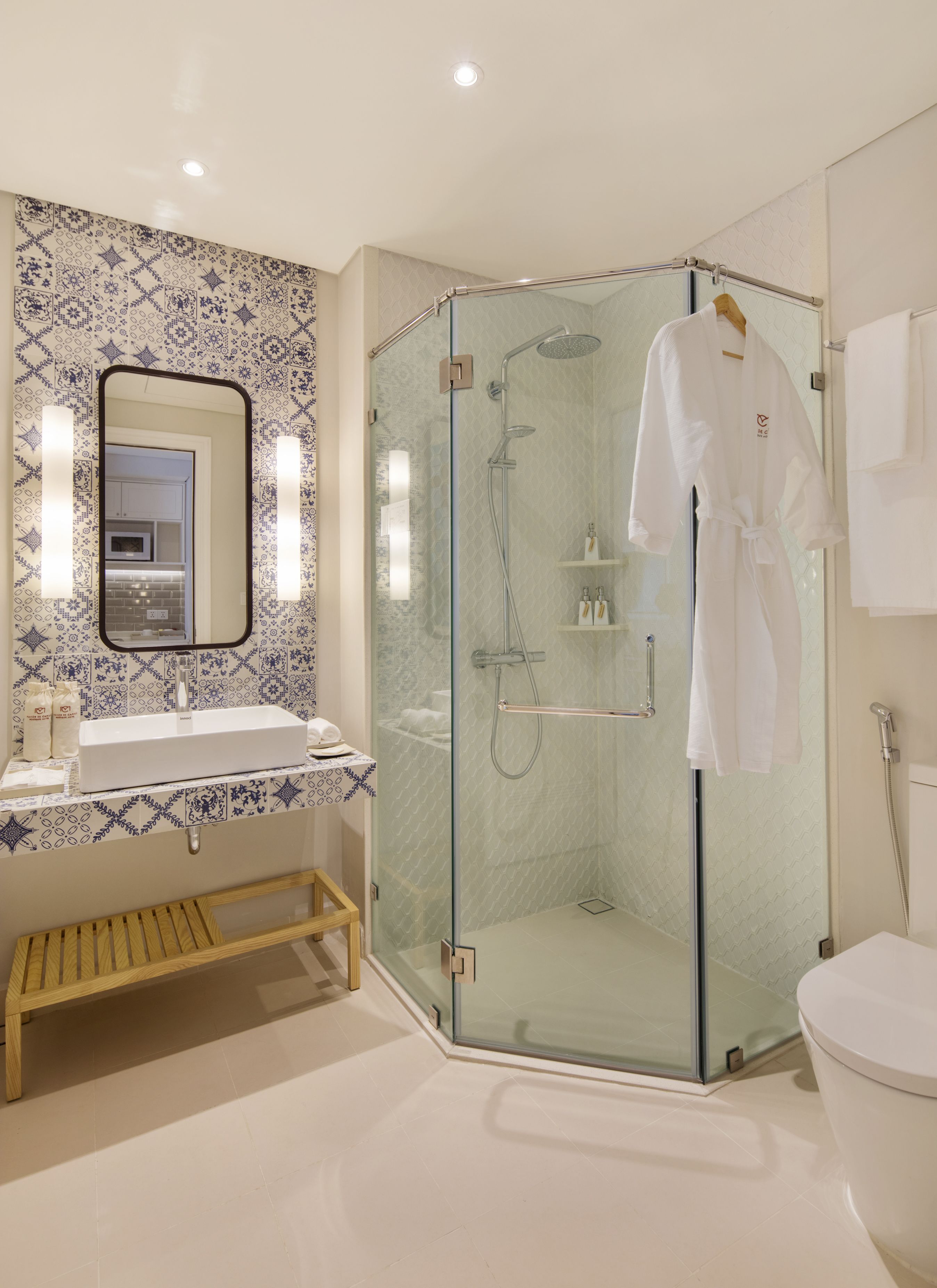 A modern bathroom with a glass-enclosed shower, a white sink, and a wooden bench.