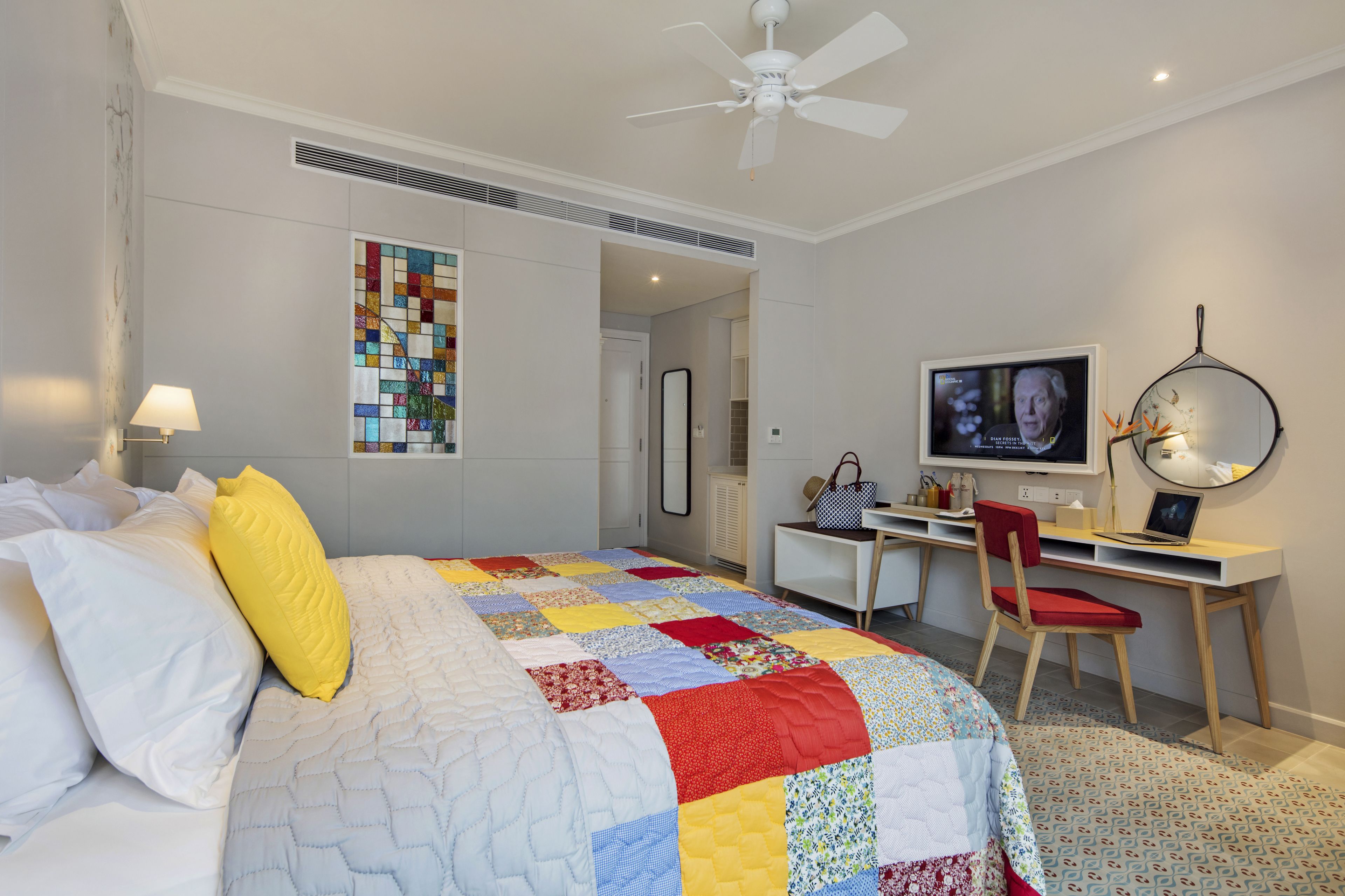 Un dormitorio con cama, escritorio, silla, televisor y ventilador de techo.