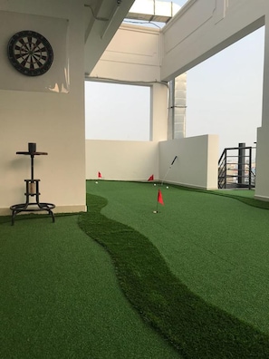 A room with artificial turf, a dartboard, and a target with red flags.