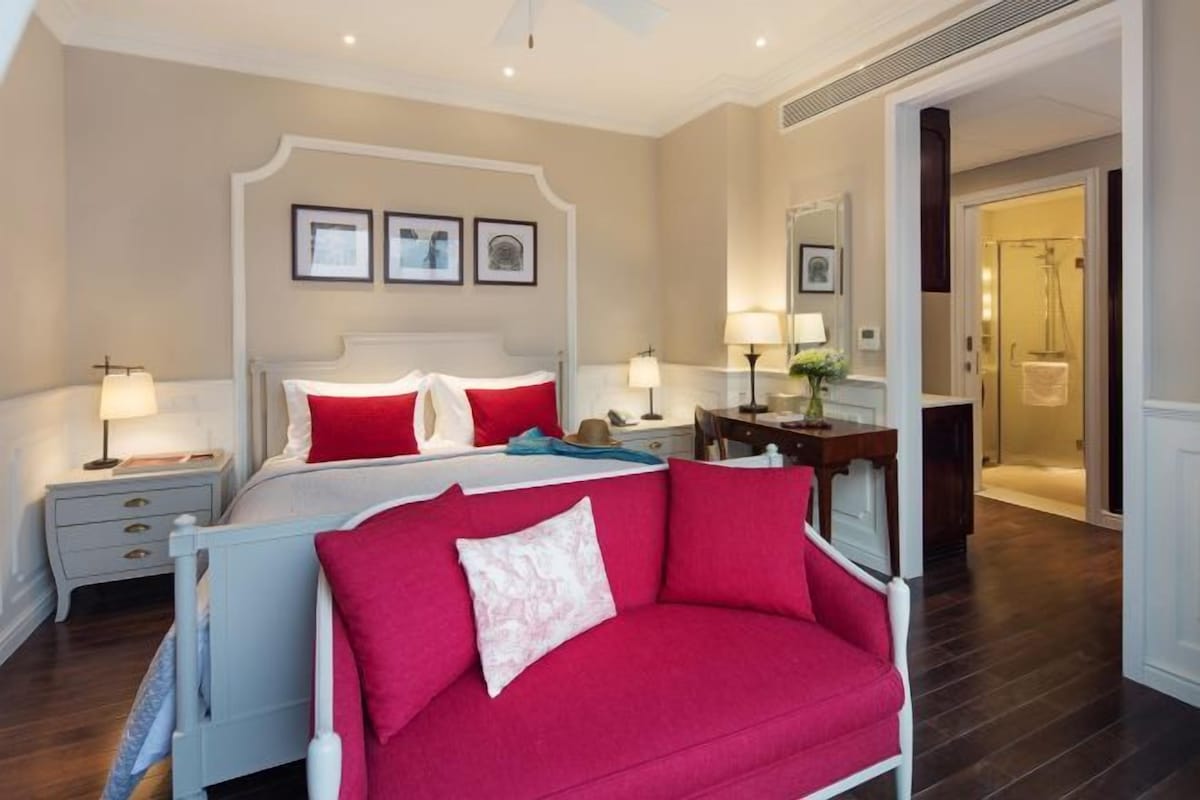 A bedroom with a bed, a red sofa, a nightstand, a dresser, and a mirror.
