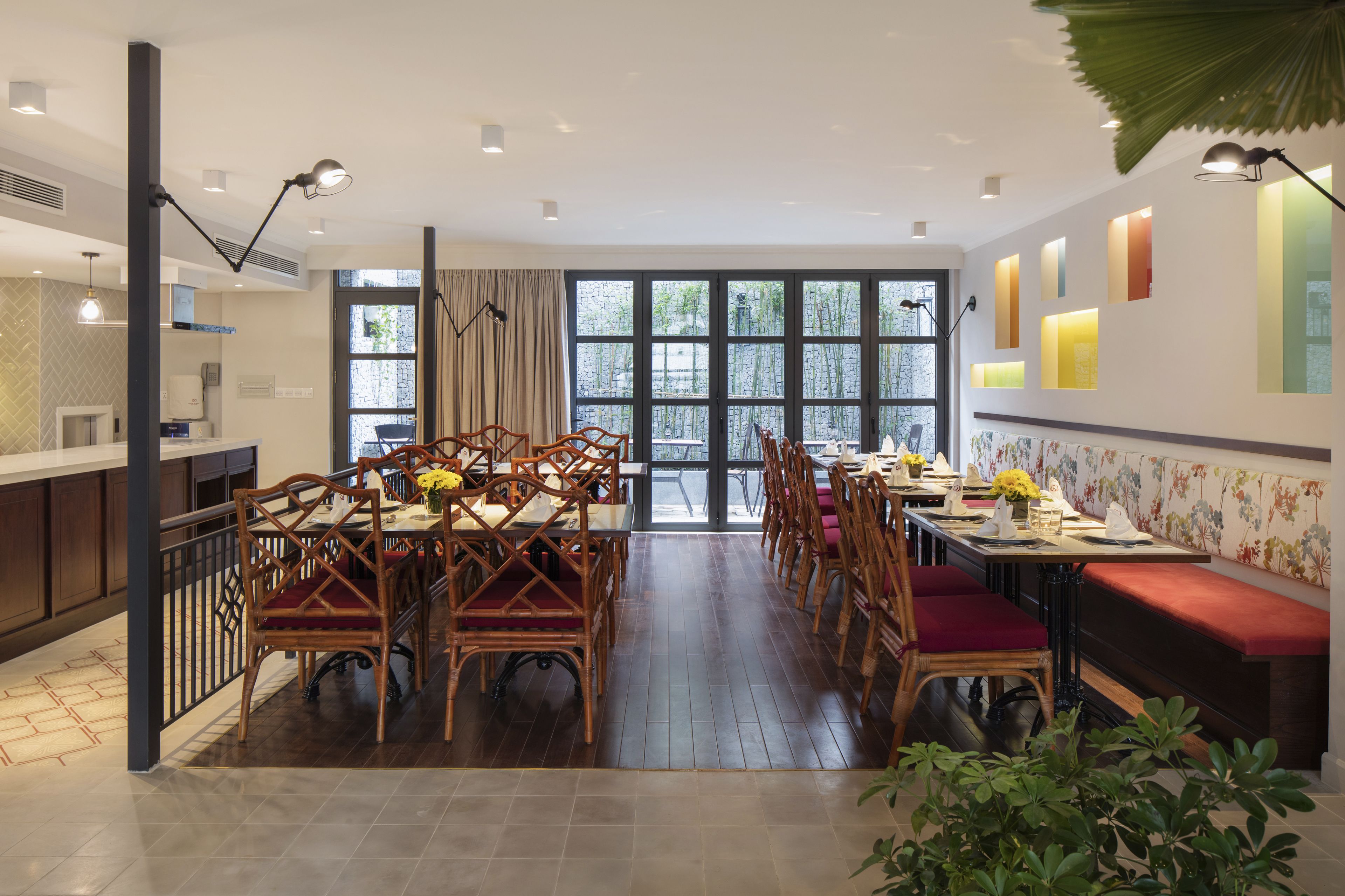 A spacious dining area with wooden tables and chairs, large windows, and a view of greenery outside.
