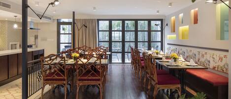 A spacious dining area with wooden tables and chairs, large windows, and a view of greenery outside.