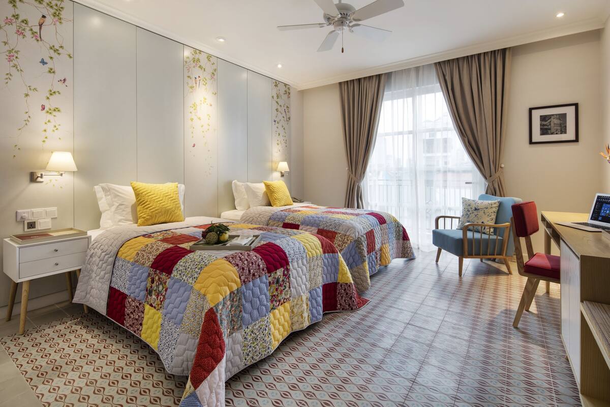 Ein Hotelzimmer mit einem großen Bett, einem Schreibtisch mit Computer, einem Sessel und einem Deckenventilator.