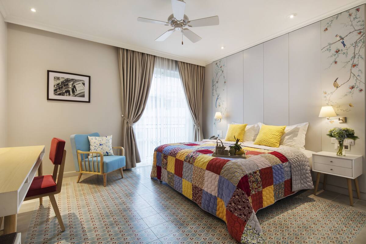 Ein helles Schlafzimmer mit einem großen Bett, einem Schreibtisch, einem Stuhl und einem Deckenventilator.