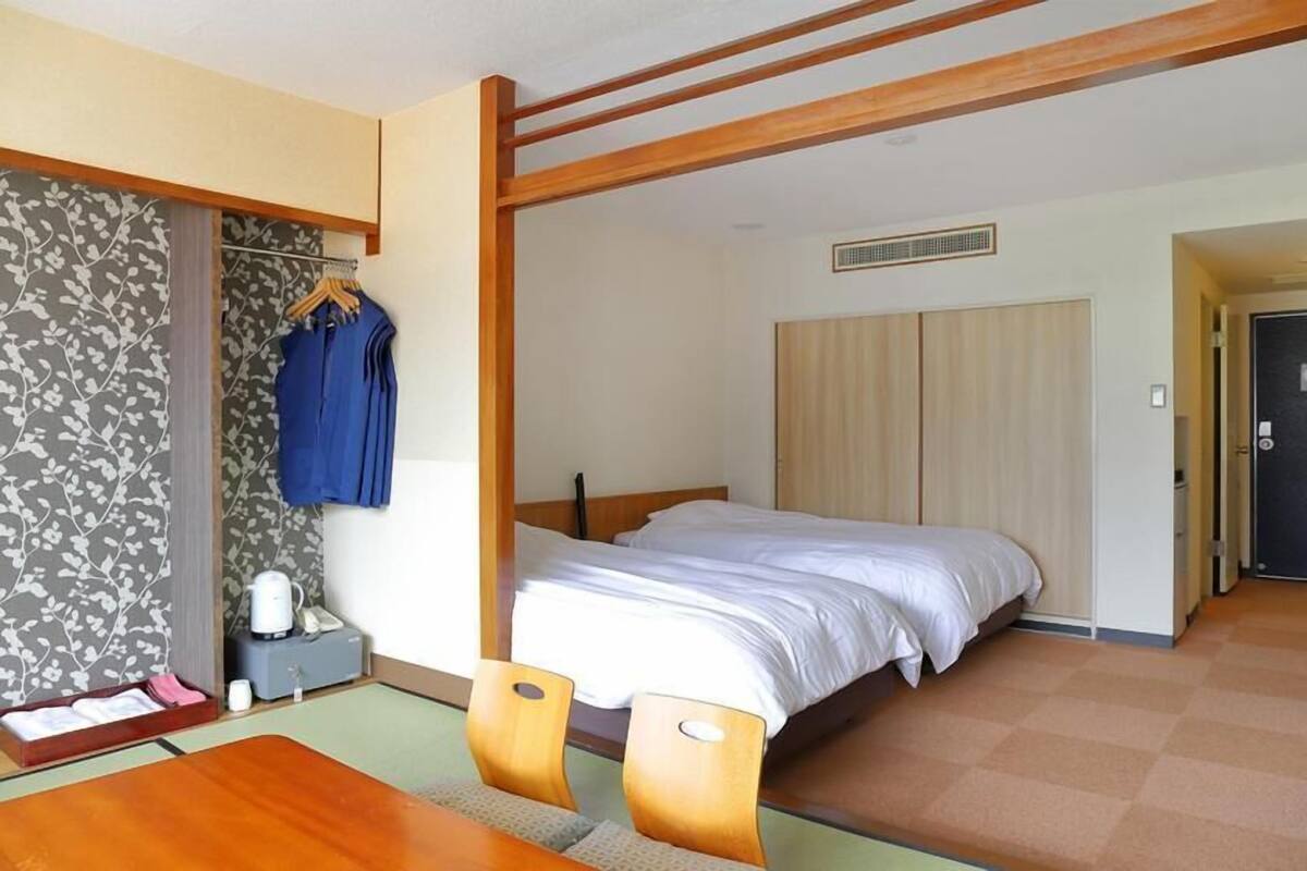 A hotel room with a bed, a wooden table, a chair, a wardrobe, and a hanging coat rack.