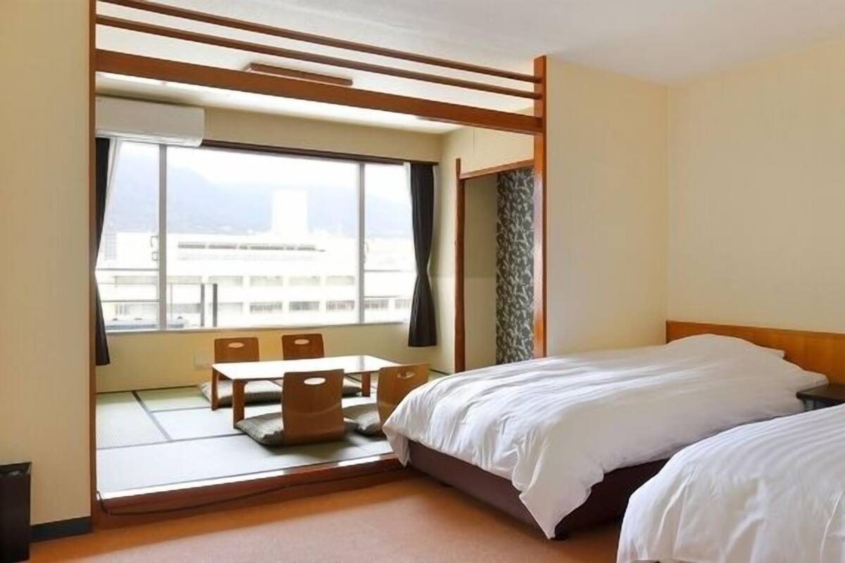 A hotel room with a bed, a small table, and a window with a view of buildings.