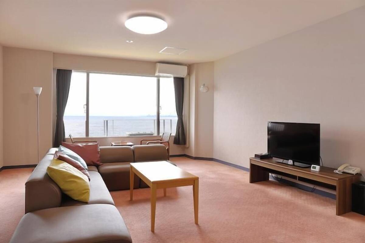 A modern living room with a sofa, a coffee table, a TV, and a view of the sea through large windows.