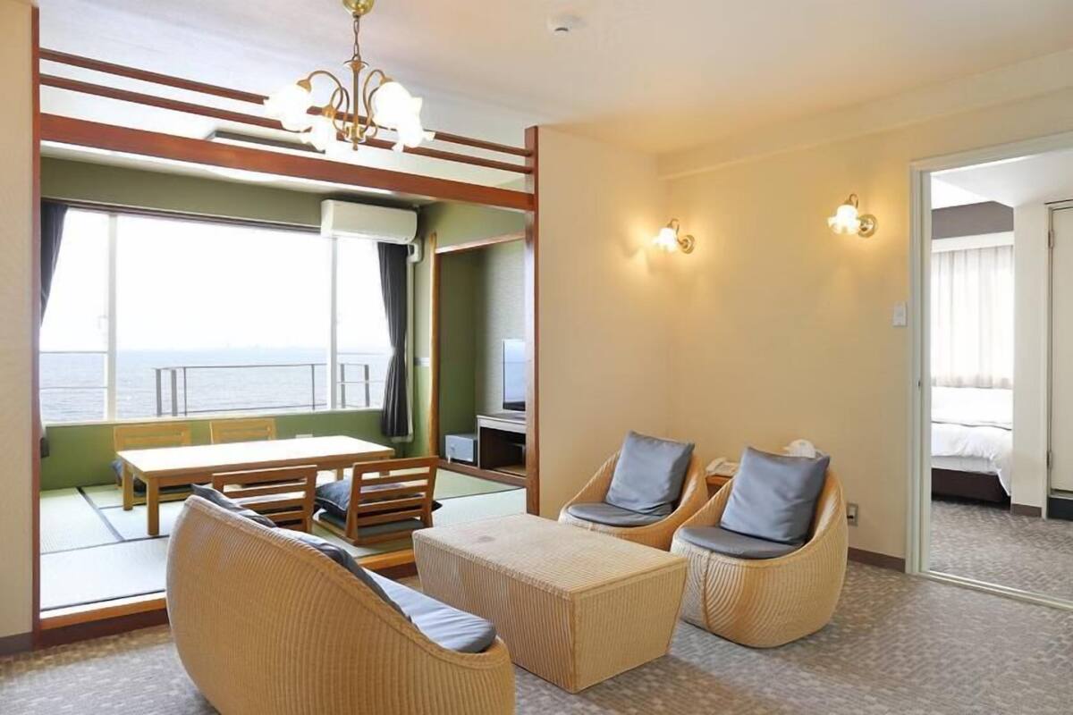 A hotel room with a balcony, wicker furniture, a television, and a bed.
