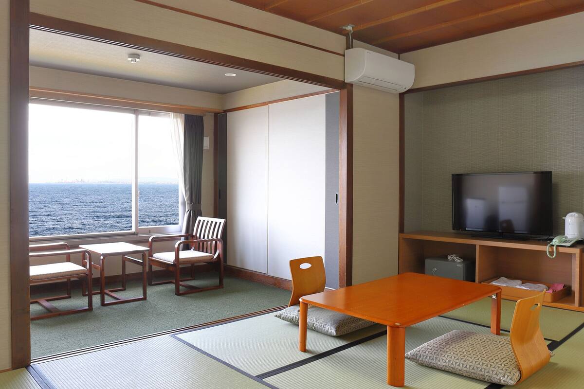A room with tatami mats, a television, a coffee maker, and a view of the sea.