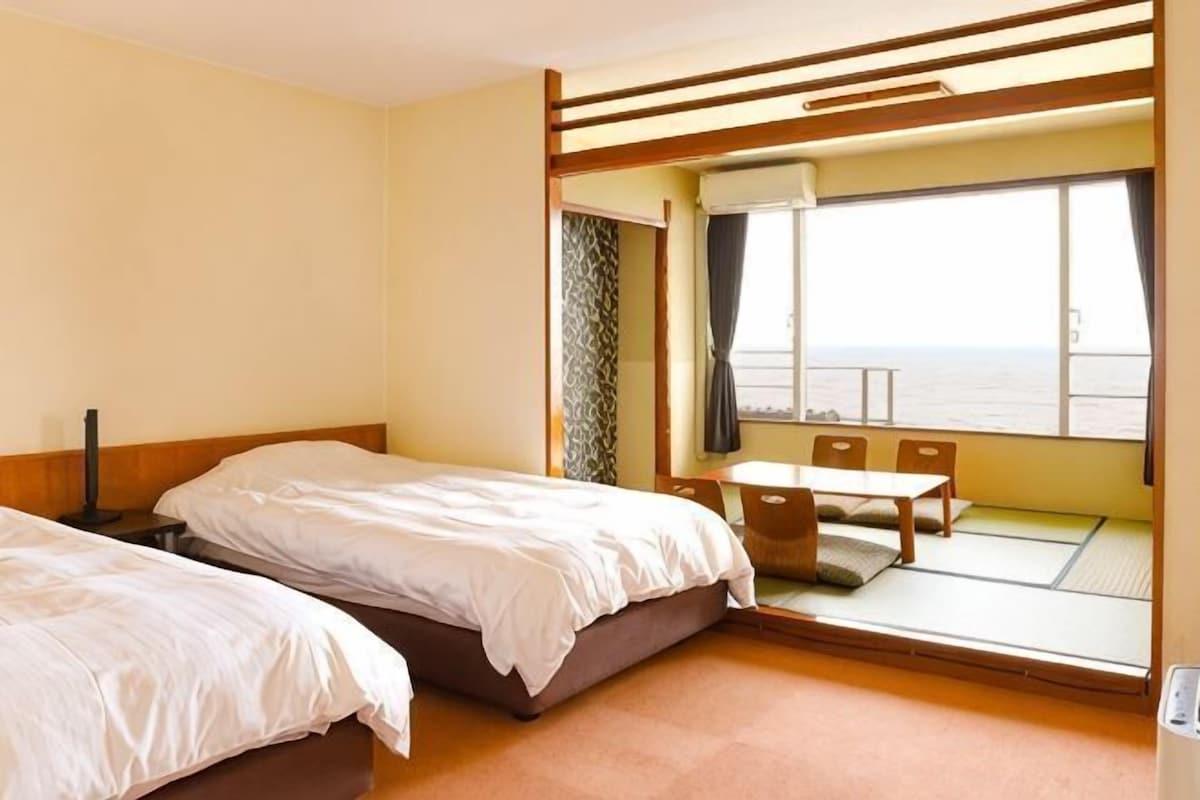 Habitación de hotel con dos camas, una mesita y vista al mar.