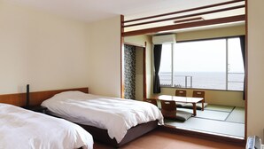 Quarto de hotel com duas camas, uma mesinha e vista para o mar através de uma grande janela.
