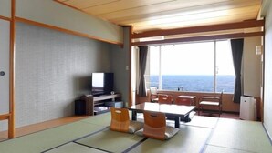 Quarto com tatames, televisão, mesa, cadeiras e vista para o mar.