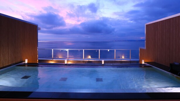 Área de piscina com vista para o mar ao anoitecer.