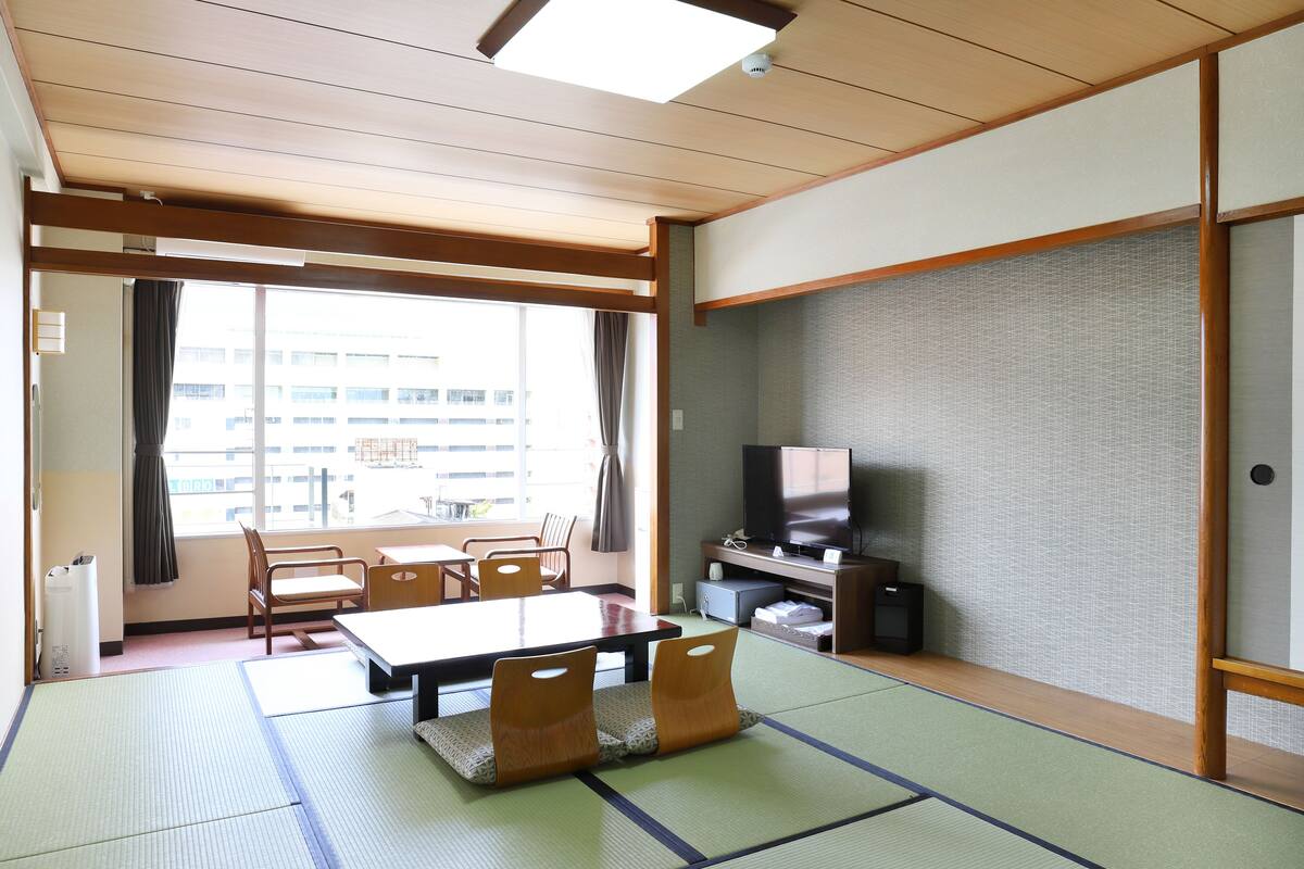 A traditional Japanese room with tatami flooring, a low table, chairs, a television, and a sliding door.