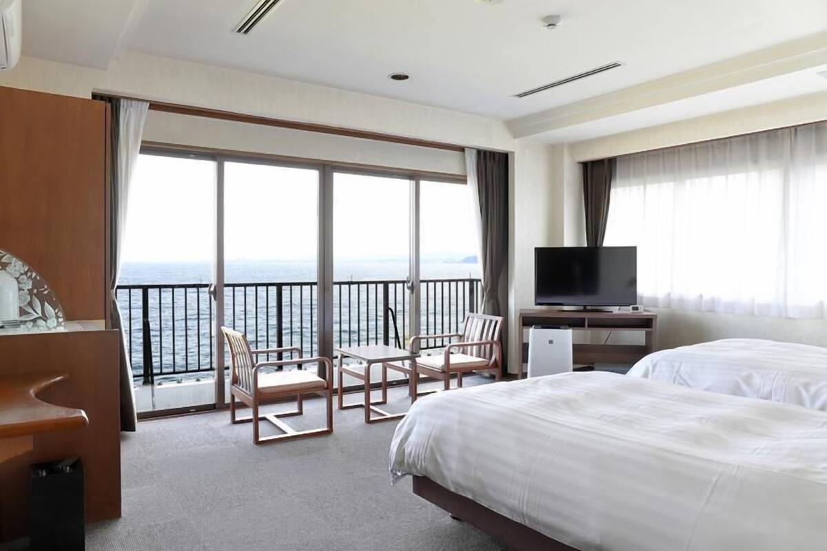 A hotel room with a large bed, a TV, a desk, and a balcony with a view of the sea.