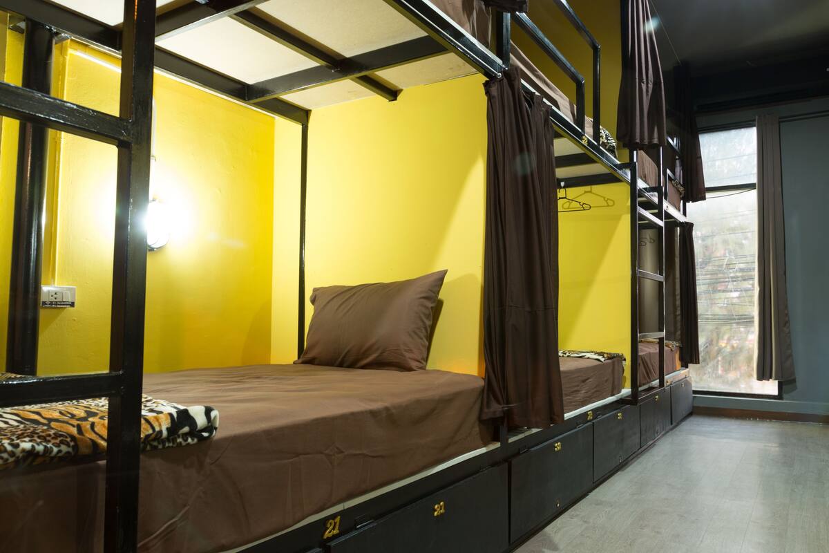 A bunk bed room with yellow walls, a window with curtains, and a bed with a brown mattress and pillow.