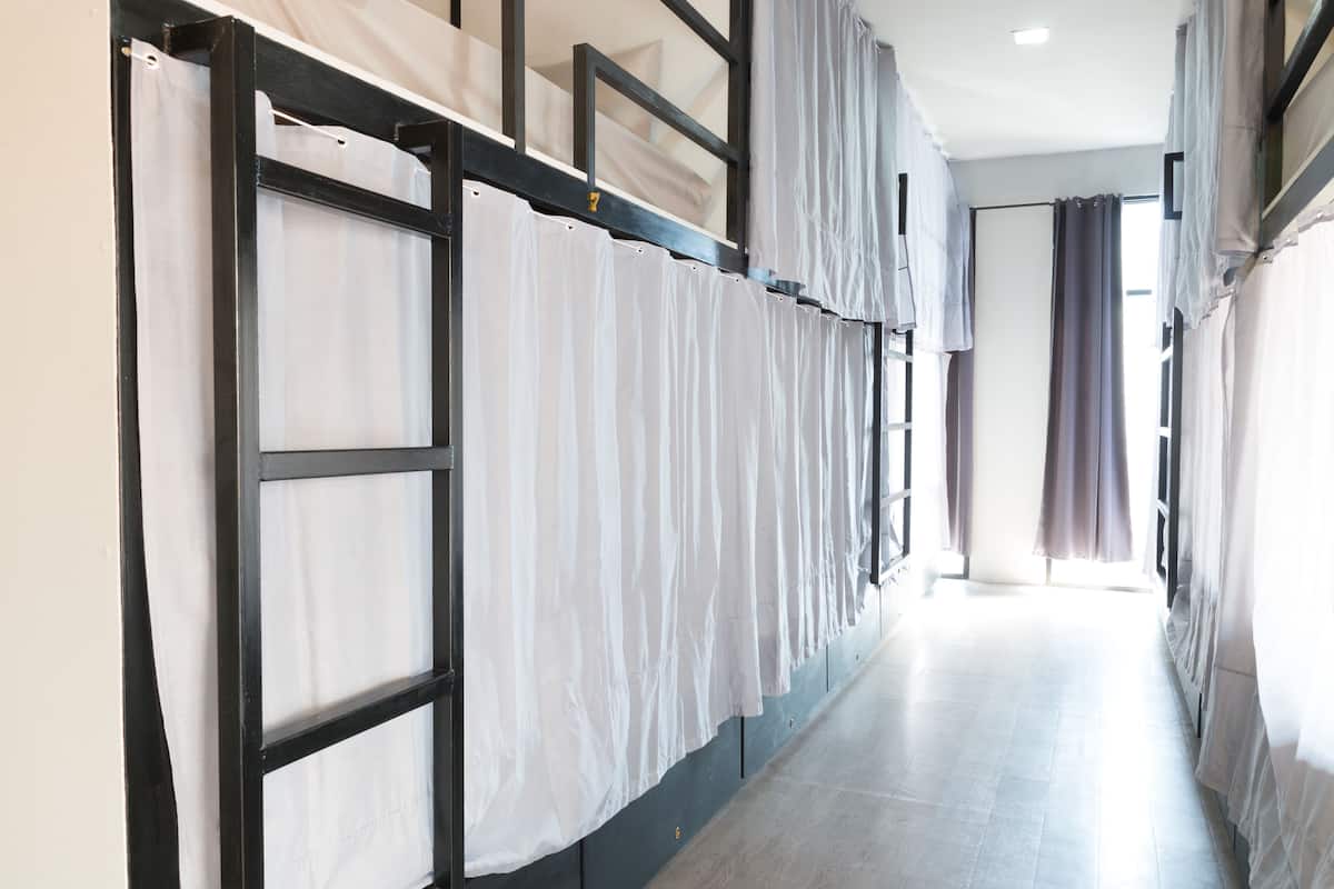 A corridor with bunk beds and curtains, leading to a room with a window.
