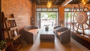 A cozy seating area with a brick wall, a large window, and a decorative metal wheel. - Iris hostel (Chiang Mai)