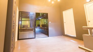 A room with a bunk bed, a glass door leading to another room, a white door, and a modern light fixture. - Iris hostel (Chiang Mai)