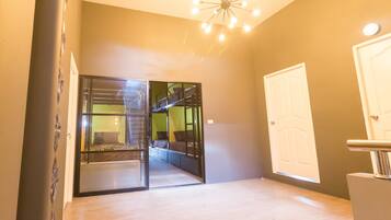 A room with a bunk bed, a glass door leading to another room, a white door, and a modern light fixture.