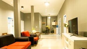 A modern living room with a sofa, ottoman, and a TV on a stand. - Iris hostel (Chiang Mai)
