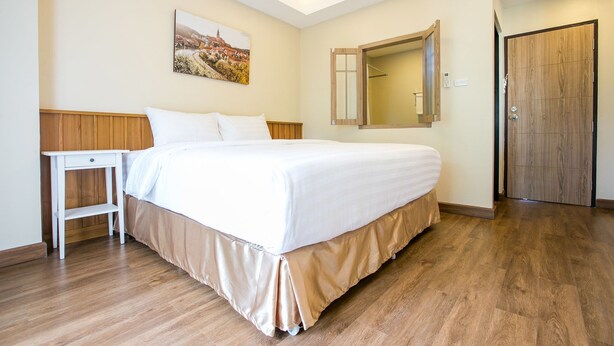 A bedroom with a large bed, a bedside table, a mirror, and a wooden door. - De Resto (Hat Yai)