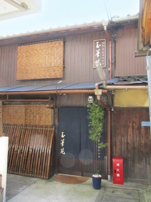A traditional Japanese building with a wooden exterior, a dark entrance door, and a bamboo fence.