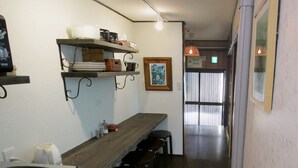 A narrow kitchen with a wooden countertop, a sink, and a shelf with kitchenware. There are stools and a framed picture on the wall. - Secret Garden Kyoto (Kyoto)