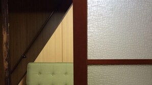 A green sofa in a corner with a wooden staircase and textured wall panels. - Secret Garden Kyoto (Kyoto)