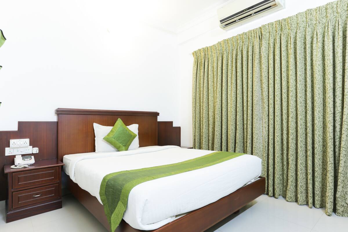 A hotel room with a wooden bed, a bedside table with a phone, a green pillow, and a green bedspread.