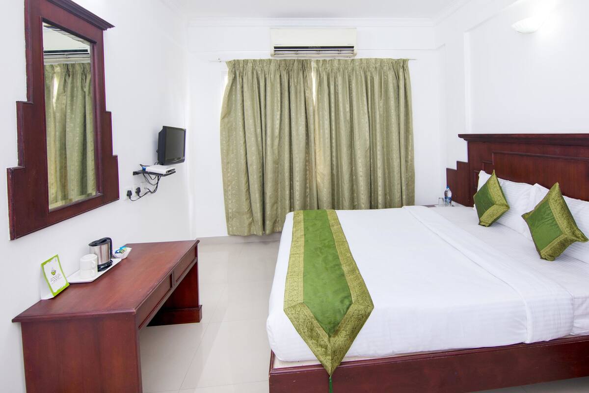 A hotel room with a bed, a desk, a television, and a window with curtains.