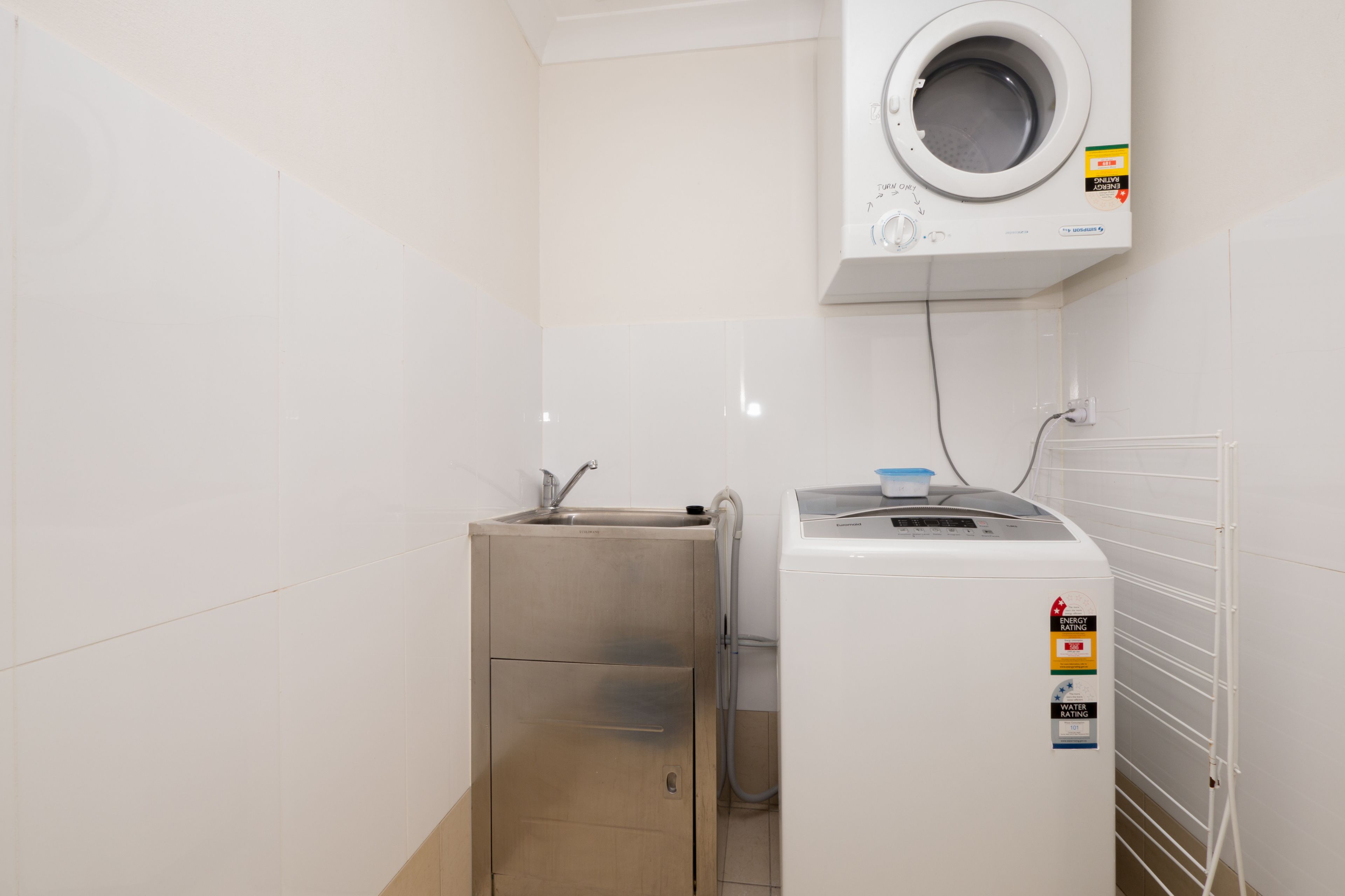 Ein kleines Badezimmer mit einem Edelstahlwaschbecken, einer wandmontierten Waschmaschine und einem kleinen Schrank.