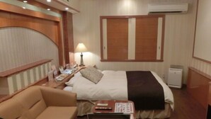 Une chambre d’hôtel comprenant un lit, une table de chevet avec une lampe, un petit bureau, une chaise et un téléviseur.