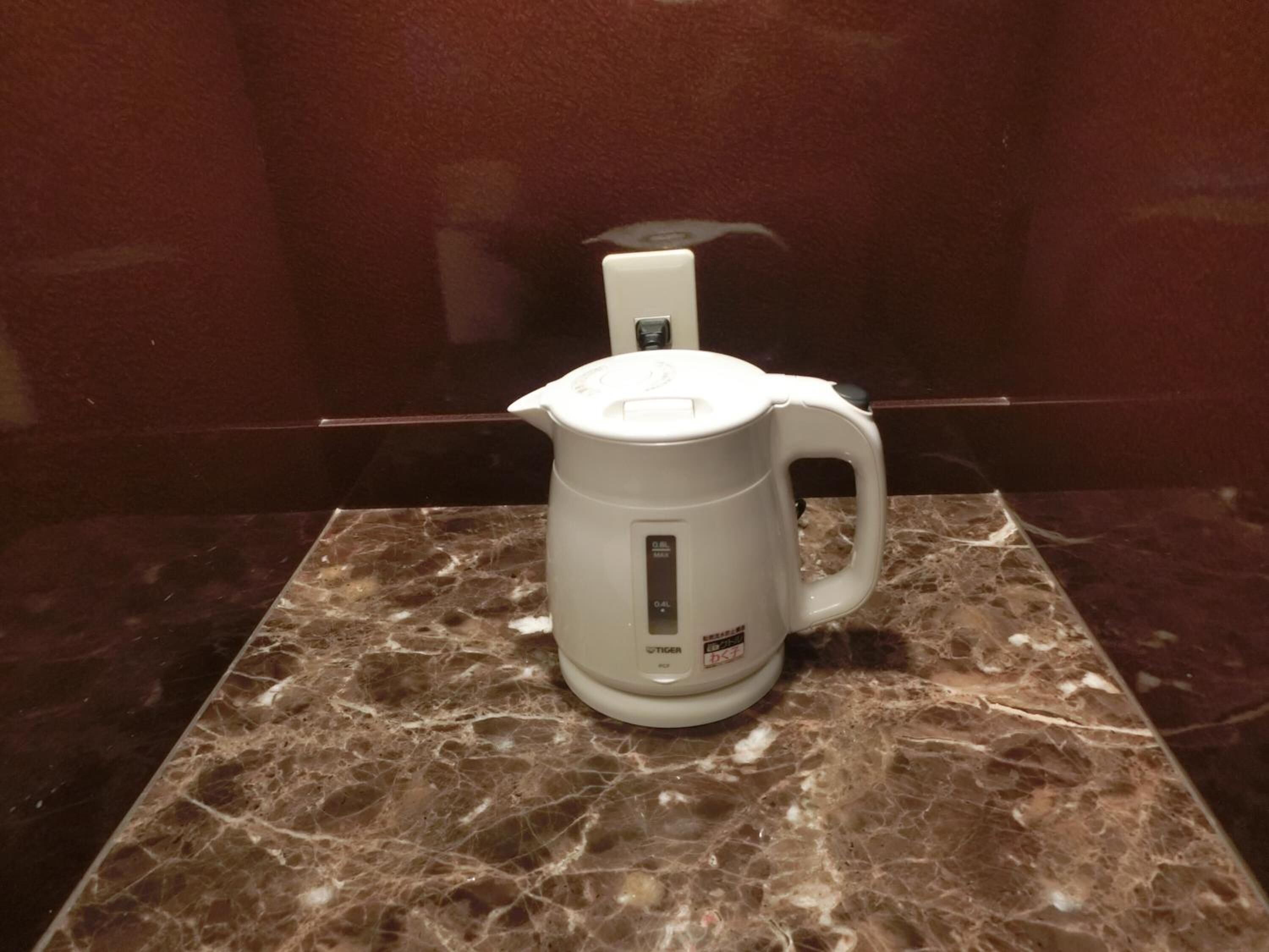 Uma chaleira elétrica branca sobre uma bancada de mármore em um banheiro.