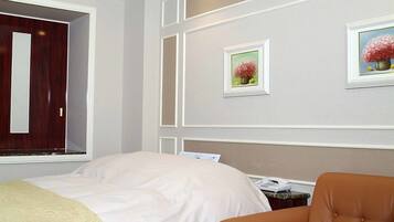 A hotel room with a bed, a brown leather sofa, a red table, and two framed floral pictures on the wall.