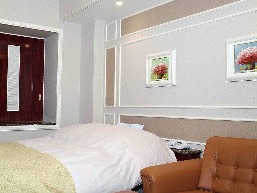 A hotel room with a bed, a brown leather sofa, a red table, and two framed floral pictures on the wall.